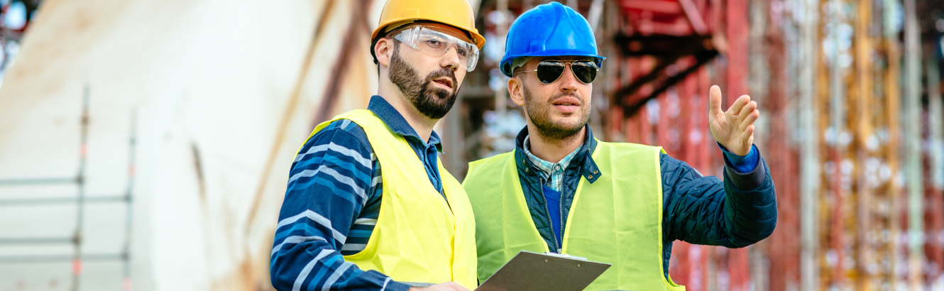 Two men in hard hats at a construction site surveying their project.